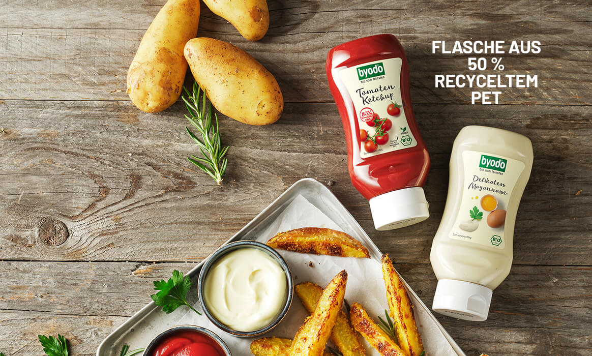 Byodo Ketchup und Mayonnaise in der Squeeze Flasche auf einem rustikalen Holzhintergrund daneben Ofenpommes und Kartoffeln